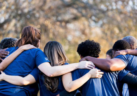 Diverse group of friends cleanup a park during a charity event. They are standing with their arms around one another.